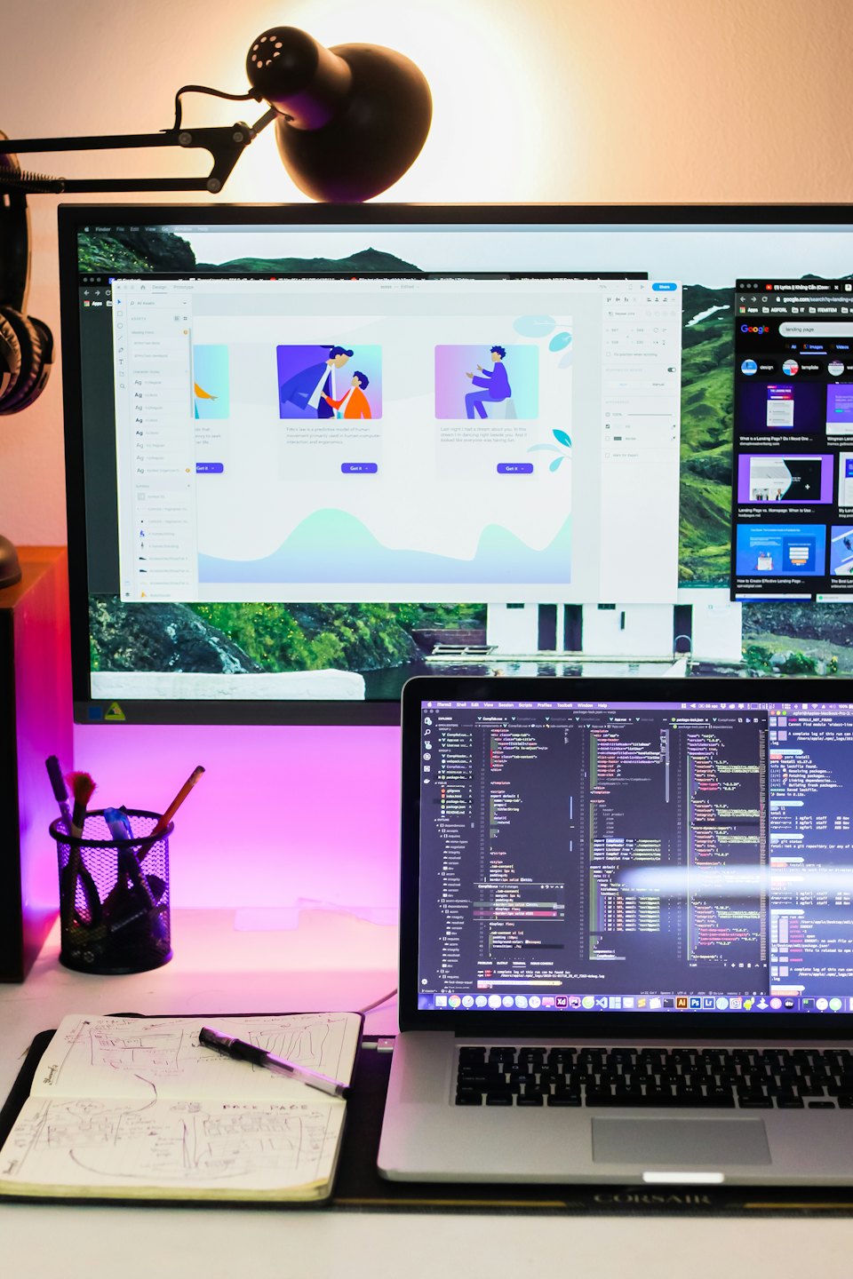 A modern desk with a computer monitor, laptop, and notebook.