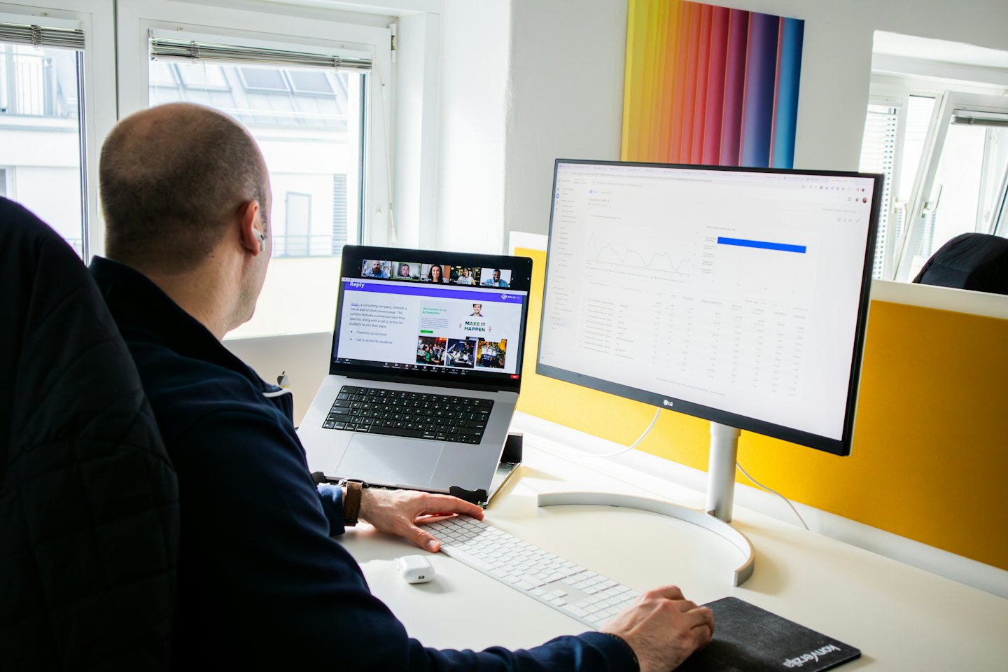 Man works on laptop and monitor in modern office.